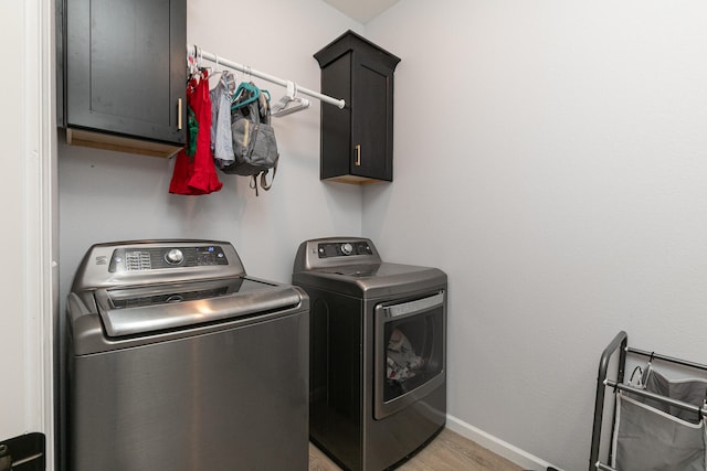 clothes washing area with washing machine and clothes dryer, light hardwood / wood-style floors, and cabinets