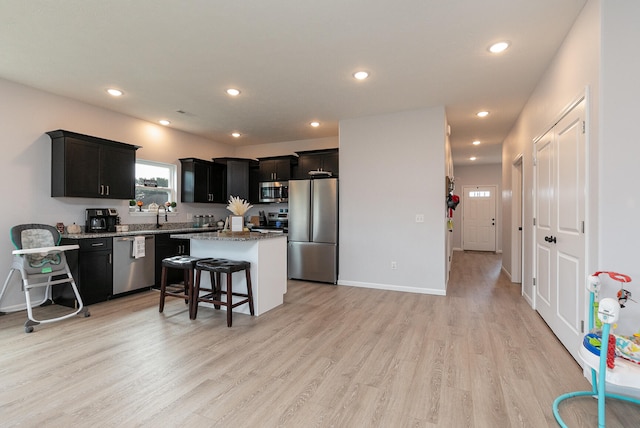 kitchen featuring light wood-type flooring, light stone counters, a center island, stainless steel appliances, and a kitchen breakfast bar