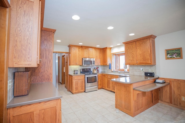 kitchen with decorative backsplash, stainless steel appliances, light tile patterned floors, kitchen peninsula, and a kitchen breakfast bar