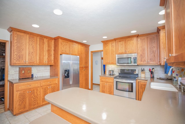 kitchen featuring backsplash, kitchen peninsula, appliances with stainless steel finishes, light tile patterned floors, and a textured ceiling