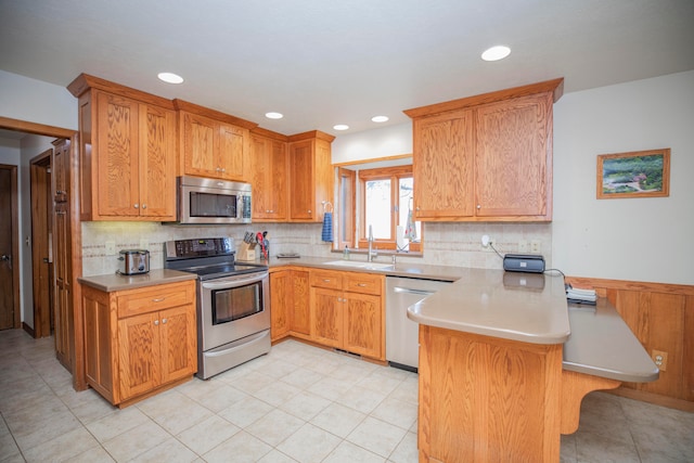 kitchen with appliances with stainless steel finishes, kitchen peninsula, sink, and tasteful backsplash