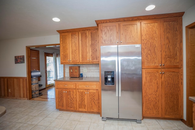 kitchen with light tile patterned flooring, tasteful backsplash, stainless steel refrigerator with ice dispenser, and wooden walls