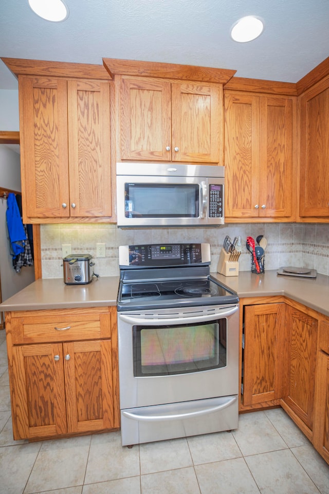 kitchen with appliances with stainless steel finishes, light tile patterned flooring, and tasteful backsplash