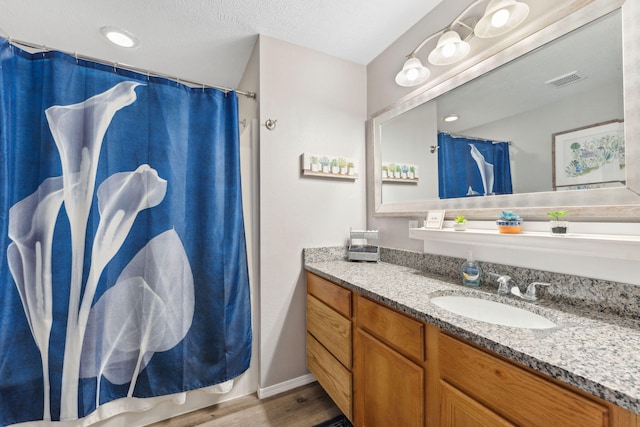 bathroom featuring hardwood / wood-style flooring, walk in shower, vanity, and a textured ceiling