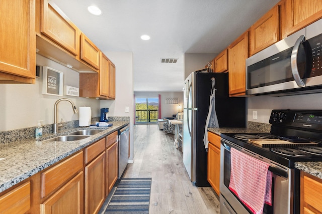 kitchen featuring appliances with stainless steel finishes, light wood-type flooring, light stone countertops, and sink