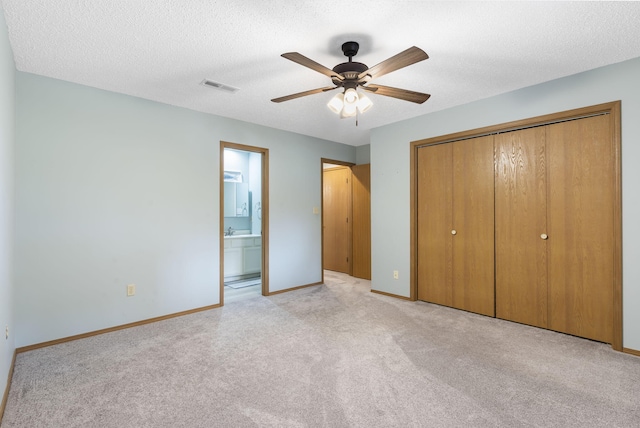 unfurnished bedroom featuring a textured ceiling, ceiling fan, a closet, ensuite bathroom, and light colored carpet