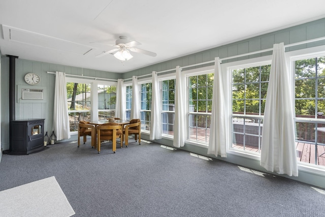 unfurnished sunroom with ceiling fan, plenty of natural light, and a wood stove