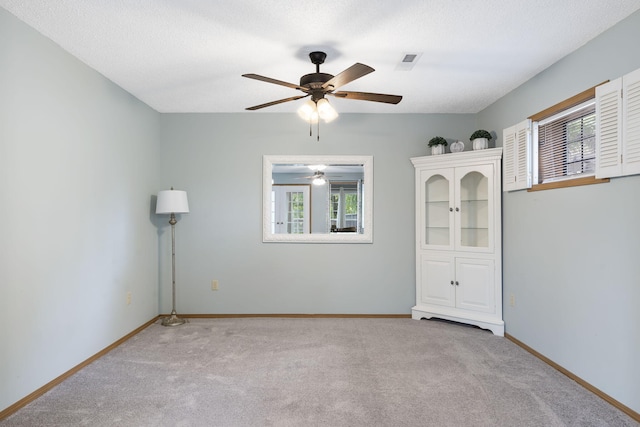 spare room featuring ceiling fan, light colored carpet, a wealth of natural light, and a textured ceiling