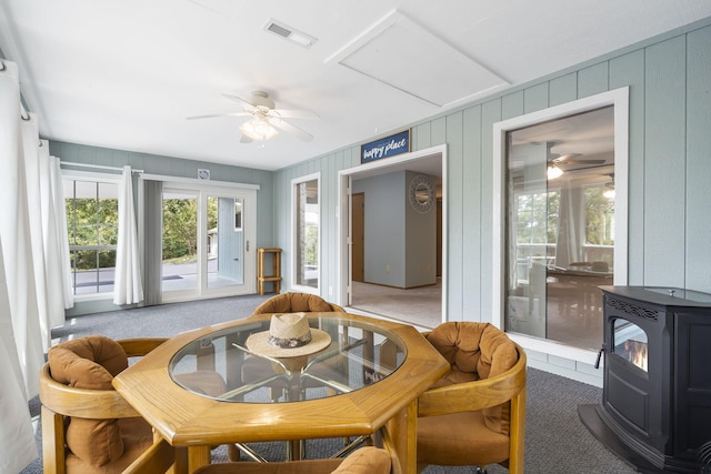 carpeted dining space with ceiling fan and a wood stove