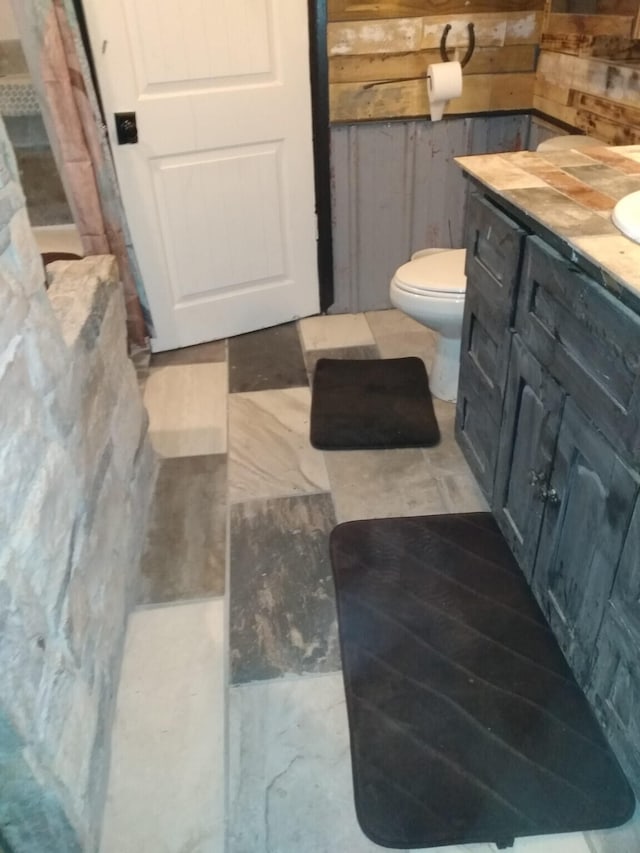 bathroom featuring curtained shower, wood walls, vanity, and toilet
