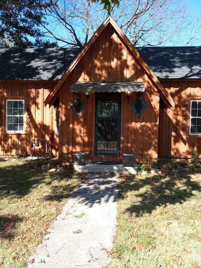 doorway to property featuring a lawn, board and batten siding, and a shingled roof