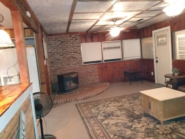 carpeted living room featuring ceiling fan, wooden walls, and a wood stove