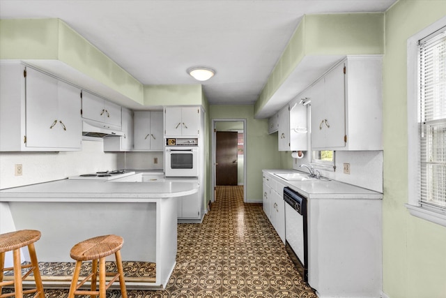 kitchen with white cabinets, white appliances, sink, kitchen peninsula, and a kitchen breakfast bar