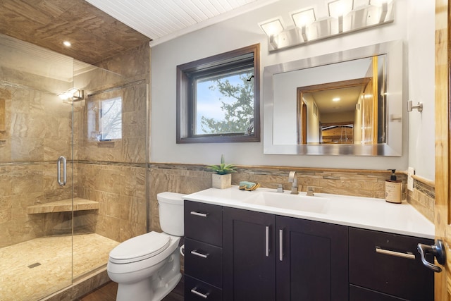 bathroom with toilet, a wainscoted wall, vanity, tile walls, and a stall shower