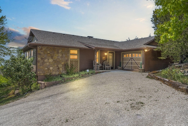 view of front of home featuring a garage, stone siding, a shingled roof, and driveway