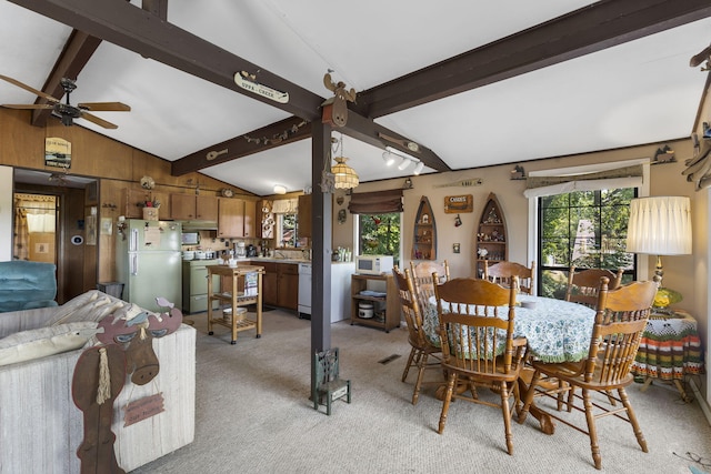 dining area featuring ceiling fan, light carpet, a healthy amount of sunlight, and vaulted ceiling with beams