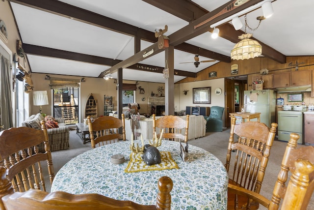 dining area with light colored carpet, lofted ceiling with beams, a warm lit fireplace, and ceiling fan