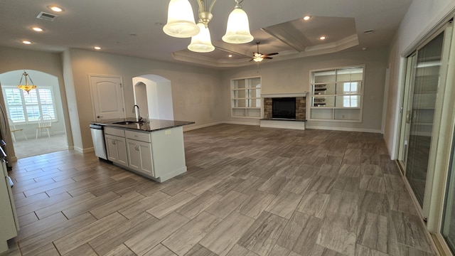 kitchen featuring a sink, arched walkways, baseboards, a fireplace, and ceiling fan with notable chandelier