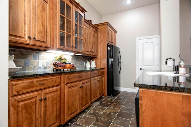 kitchen featuring tasteful backsplash, dark stone countertops, black fridge, and sink