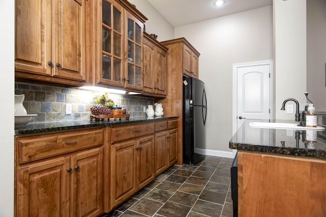 kitchen featuring baseboards, freestanding refrigerator, a sink, and glass insert cabinets