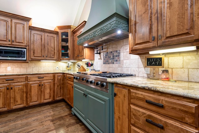 kitchen featuring light stone countertops, decorative backsplash, premium range hood, dark wood-type flooring, and appliances with stainless steel finishes