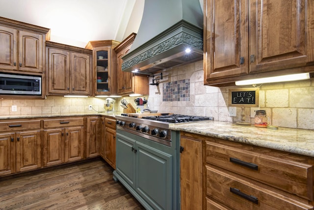 kitchen featuring light stone counters, stainless steel appliances, premium range hood, dark wood-type flooring, and tasteful backsplash