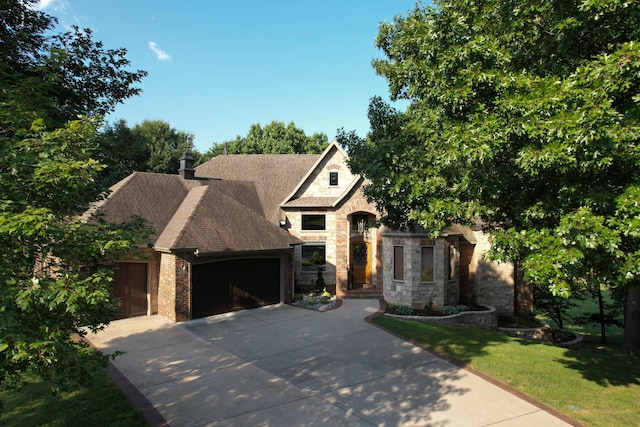 view of front facade with a garage, driveway, stone siding, a shingled roof, and a front yard