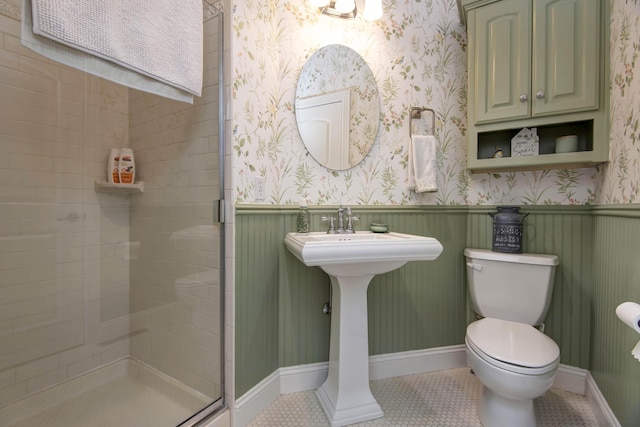 bathroom with wallpapered walls, a stall shower, a wainscoted wall, toilet, and tile patterned flooring