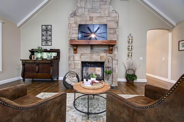living room with arched walkways, vaulted ceiling, baseboards, wood finished floors, and a stone fireplace