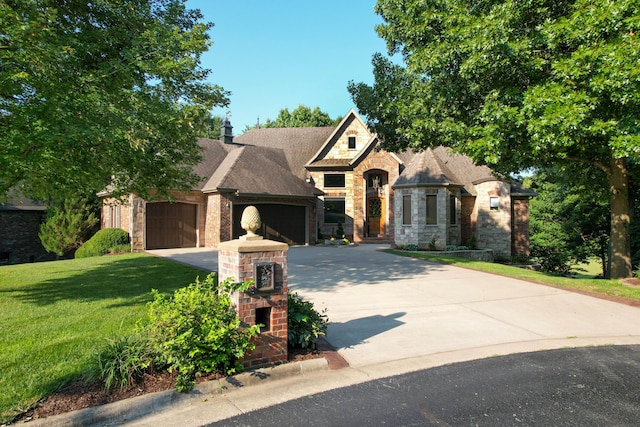 french country inspired facade featuring a garage, driveway, stone siding, and a front yard