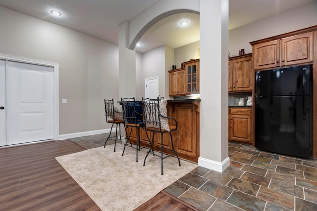 kitchen with decorative backsplash, dark hardwood / wood-style flooring, black refrigerator, and a kitchen breakfast bar