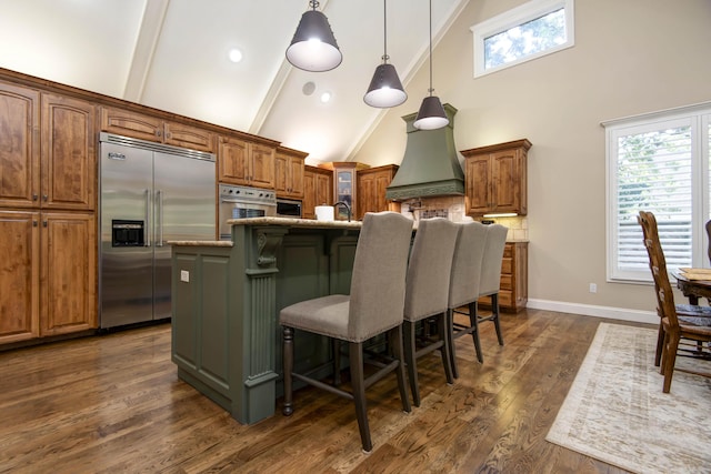 kitchen with high vaulted ceiling, brown cabinets, appliances with stainless steel finishes, and a kitchen island with sink