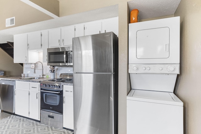 kitchen featuring stacked washer and clothes dryer, sink, decorative backsplash, appliances with stainless steel finishes, and white cabinetry