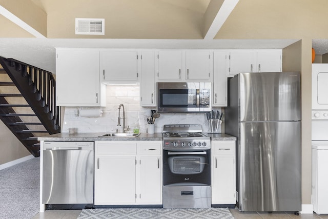 kitchen featuring sink, white cabinetry, appliances with stainless steel finishes, stacked washer / drying machine, and backsplash