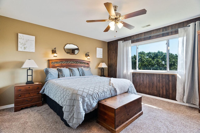 carpeted bedroom with ceiling fan and wood walls