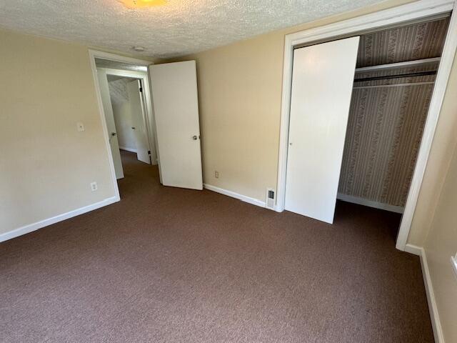 unfurnished bedroom with a textured ceiling, a closet, and dark colored carpet