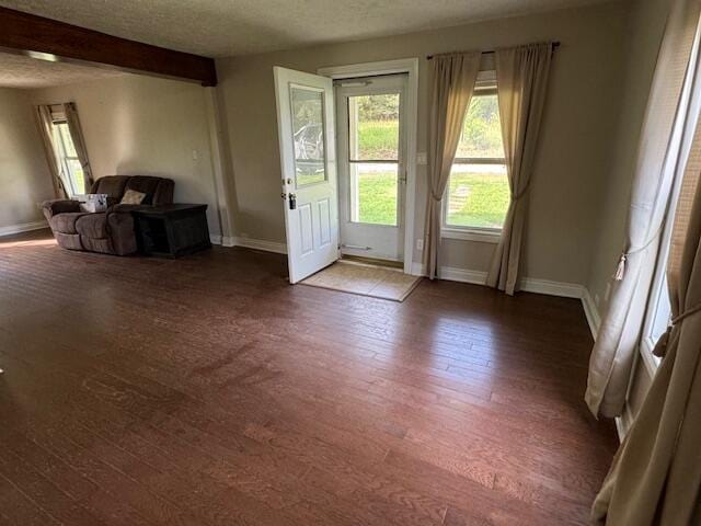 doorway to outside with a textured ceiling, beam ceiling, and dark hardwood / wood-style flooring