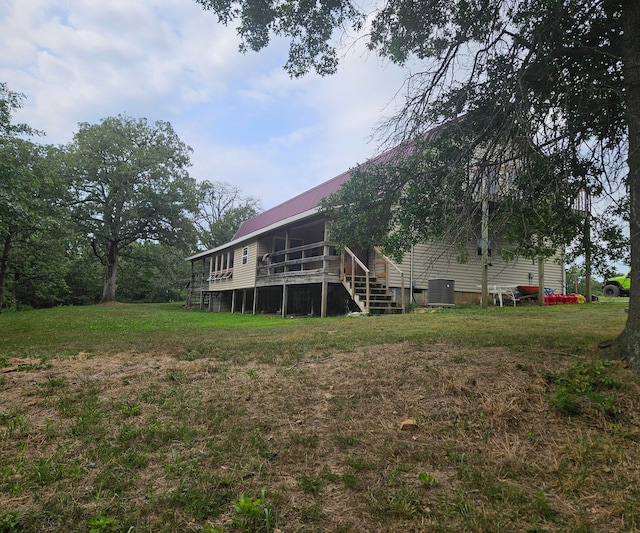 rear view of house with central AC unit, a wooden deck, and a lawn