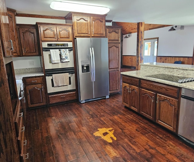 kitchen featuring light stone countertops, dark hardwood / wood-style floors, crown molding, appliances with stainless steel finishes, and wood walls