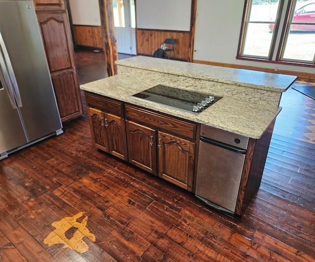 kitchen with stainless steel fridge, wood walls, a kitchen island, black electric stovetop, and dark hardwood / wood-style flooring