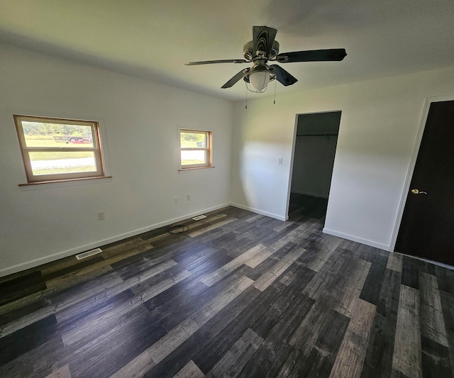 unfurnished bedroom featuring a closet, dark hardwood / wood-style floors, a walk in closet, and ceiling fan