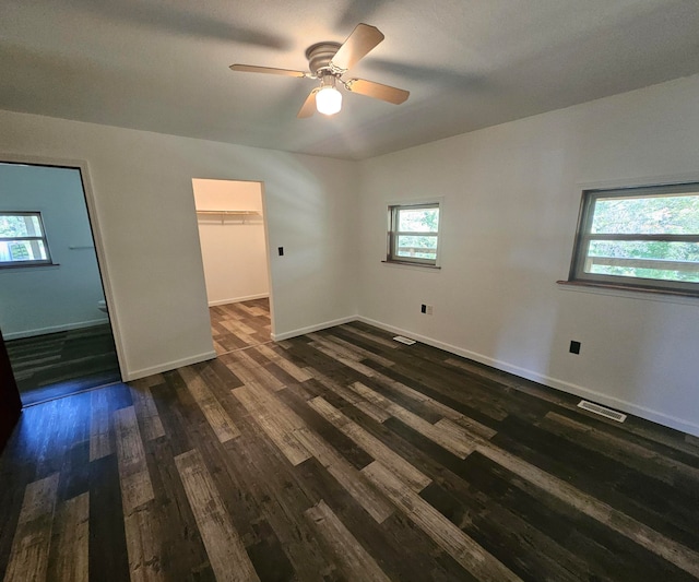 unfurnished bedroom with dark hardwood / wood-style flooring, ceiling fan, a closet, and a walk in closet