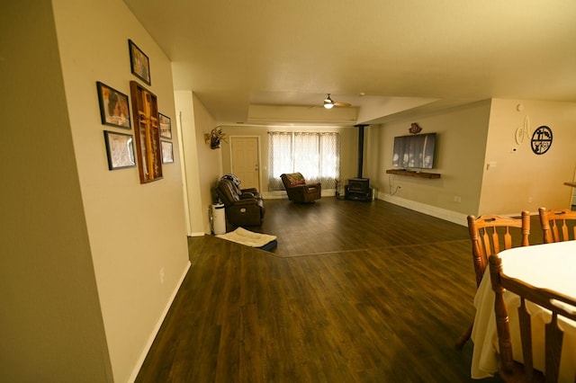 living area with a wood stove, ceiling fan, baseboards, and wood finished floors