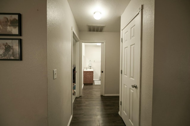 hallway featuring dark wood-style floors, baseboards, visible vents, and a textured wall