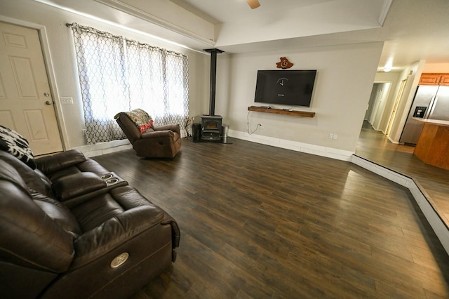 living room featuring a ceiling fan, dark wood-style flooring, a wood stove, and baseboards