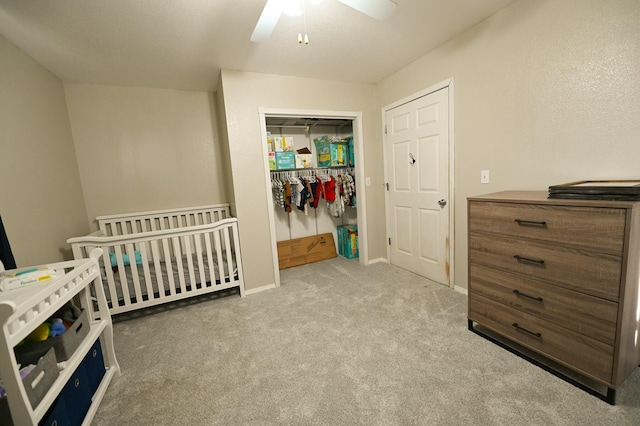 bedroom featuring a crib, baseboards, a ceiling fan, carpet floors, and a closet