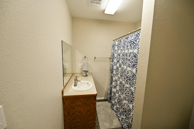 full bath featuring a shower with shower curtain, a textured wall, visible vents, and vanity