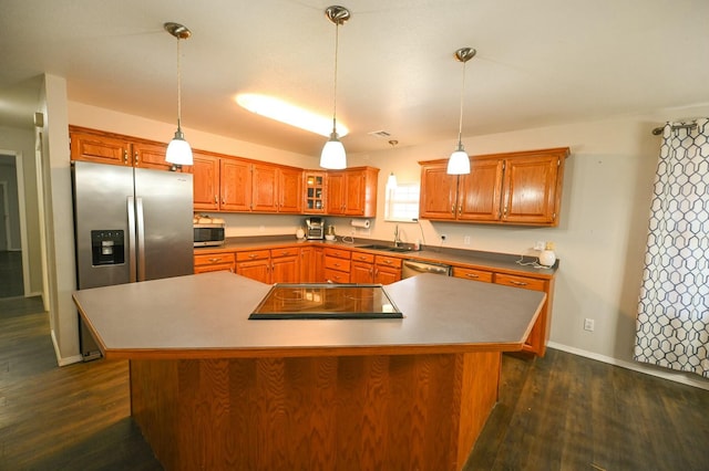 kitchen featuring dark wood-type flooring, a sink, appliances with stainless steel finishes, a center island, and brown cabinetry