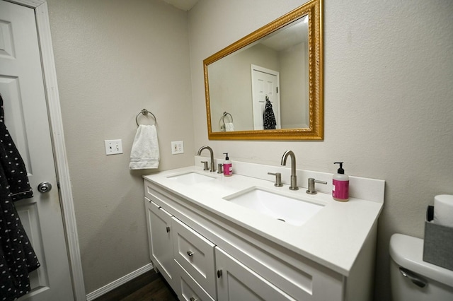 bathroom with baseboards, a sink, toilet, and double vanity