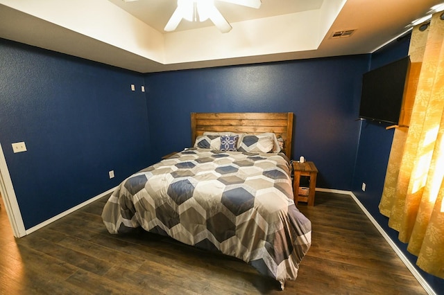 bedroom with a tray ceiling, baseboards, visible vents, and wood finished floors